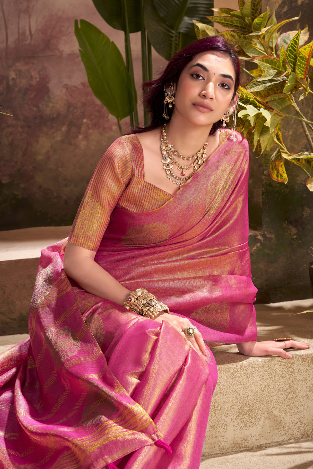 Model sitting in dark pink tissue silk saree with zari weaving butta highlighting graceful drape and rich texture