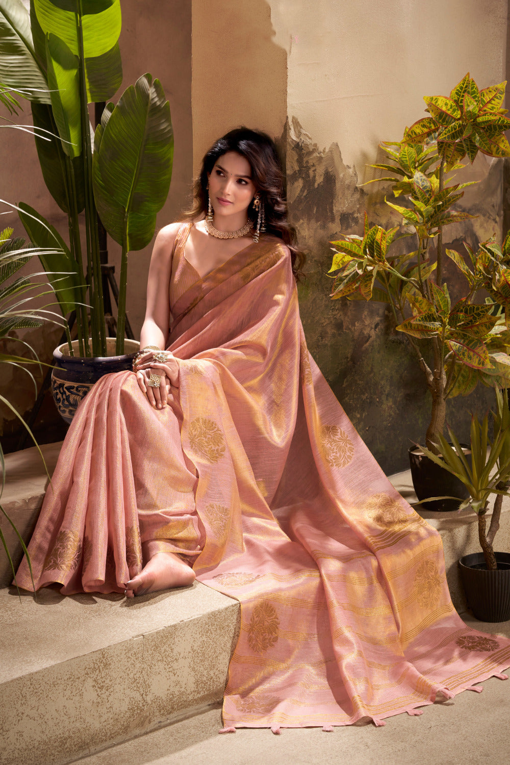 Model sitting in pink tissue silk saree with zari weaving butta highlighting graceful drape and rich texture