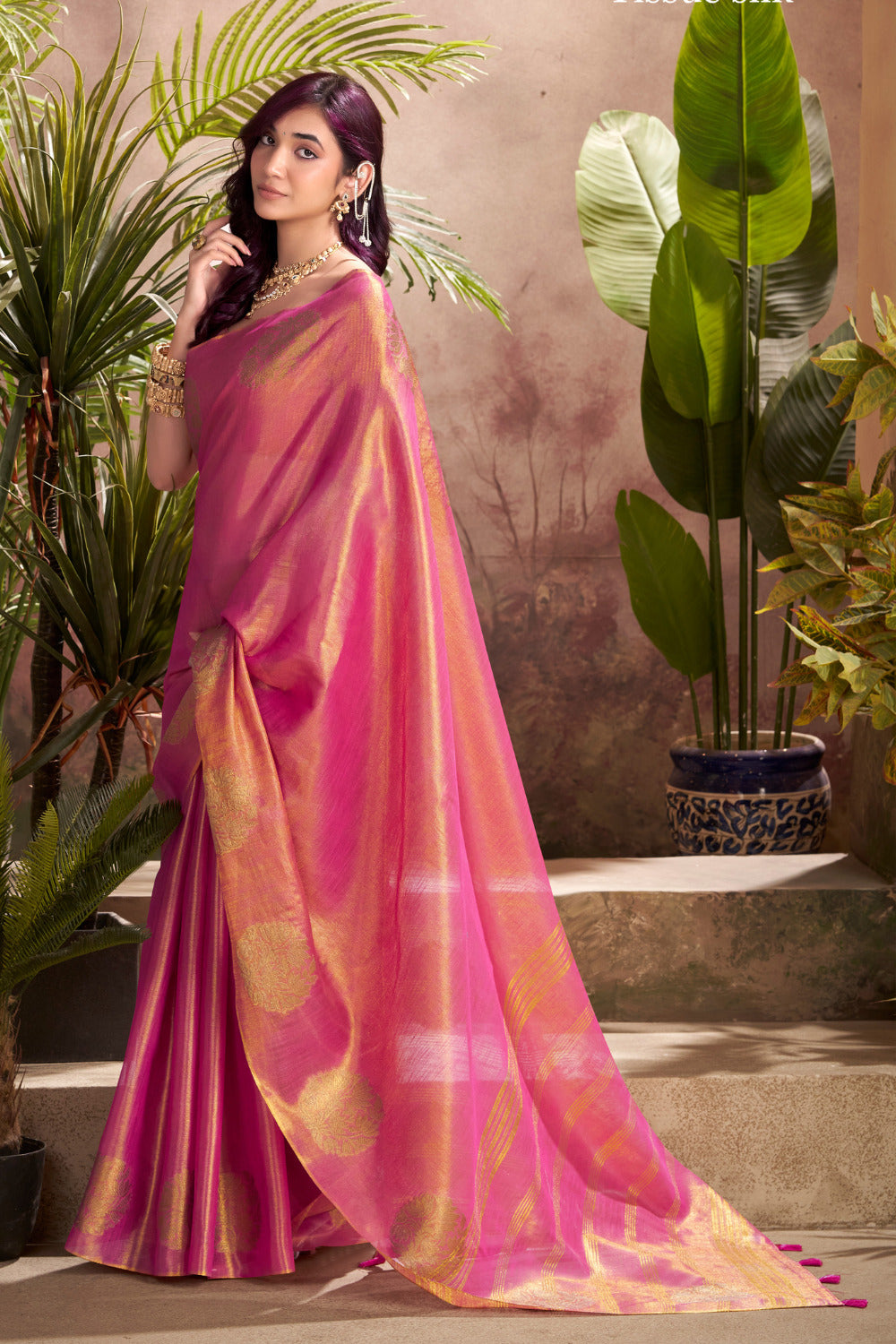 Model posing in dark pink tissue silk saree with zari butta and border pallu showing full length party and wedding styling